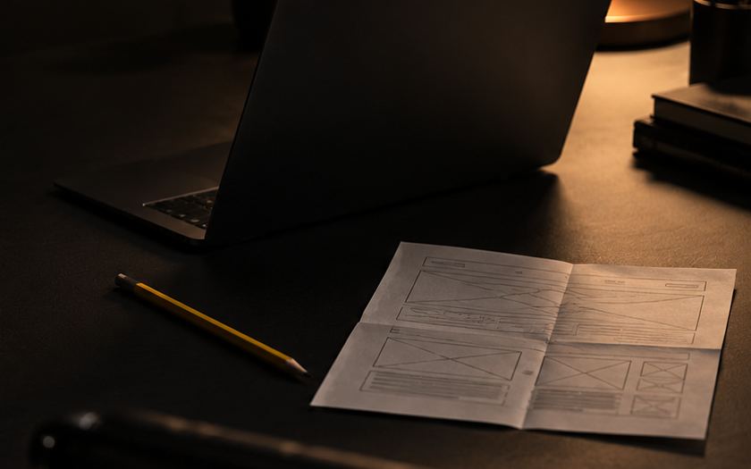 Laptop and a paper wireframe on a dark desk